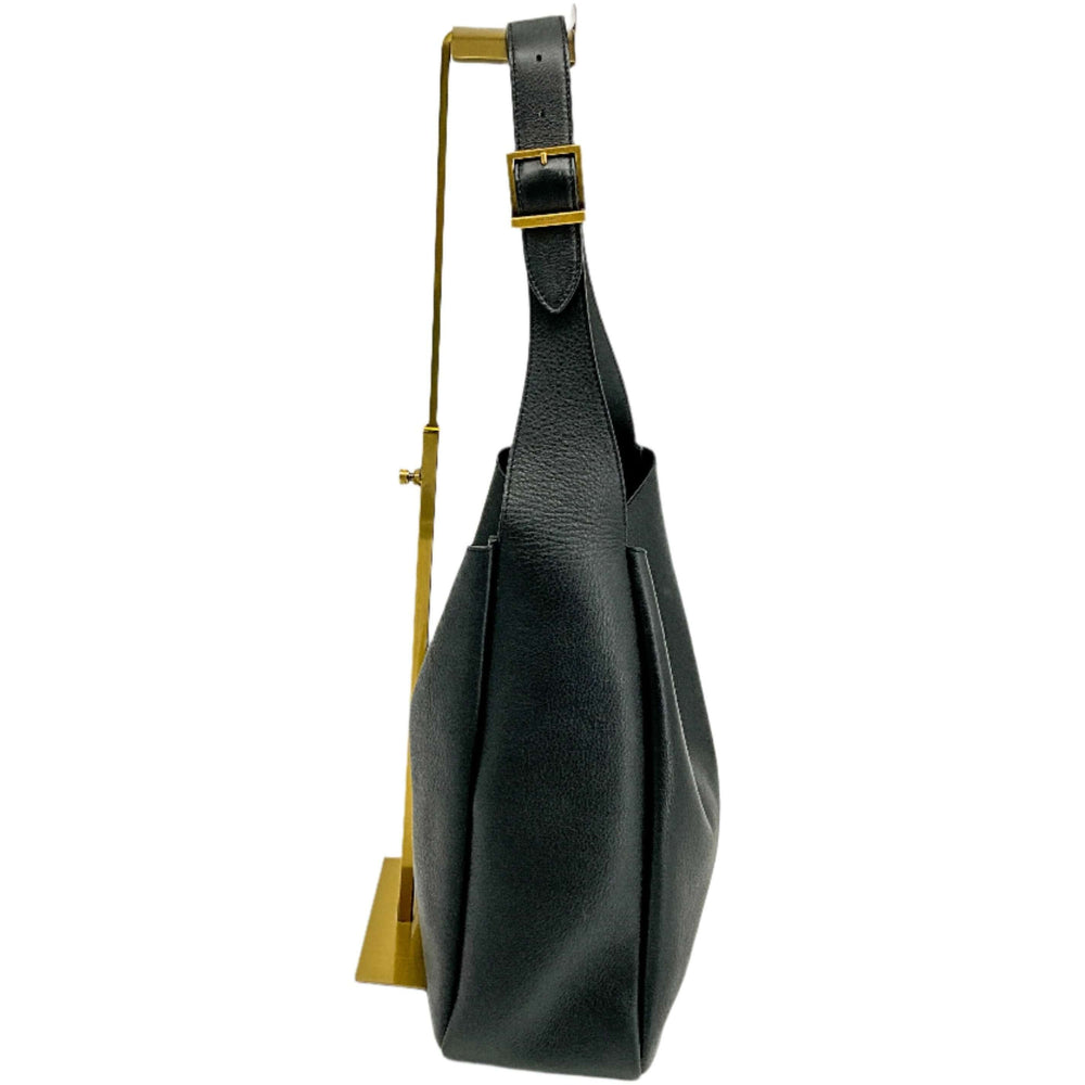 Black YSL Le 5 à 7 Large handbag hanging on a gold display stand, showcasing its side view and sleek leather design.