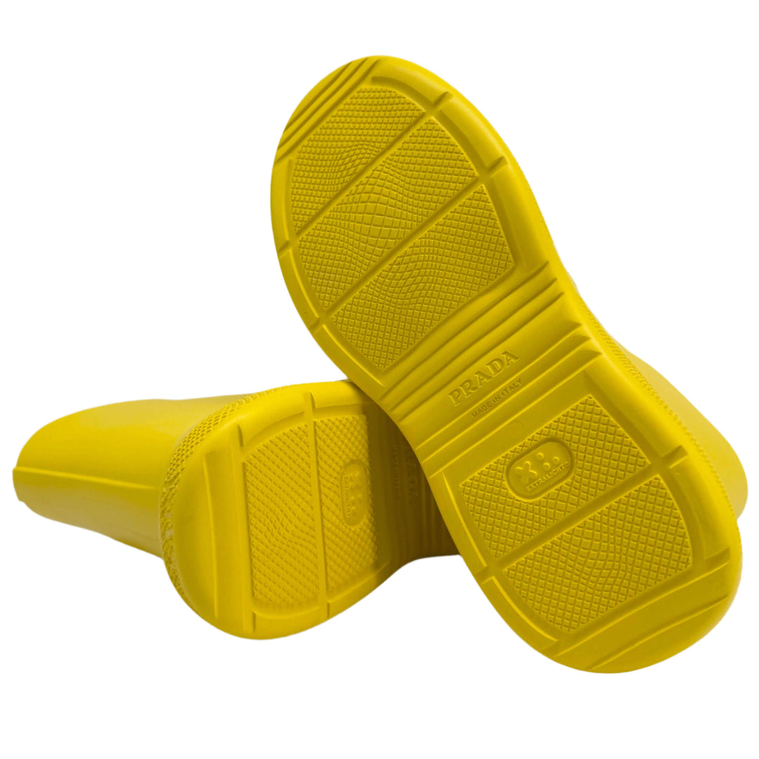 Bottom view of authentic Prada yellow rubber rain boots, highlighting slip-resistant soles and iconic branding.