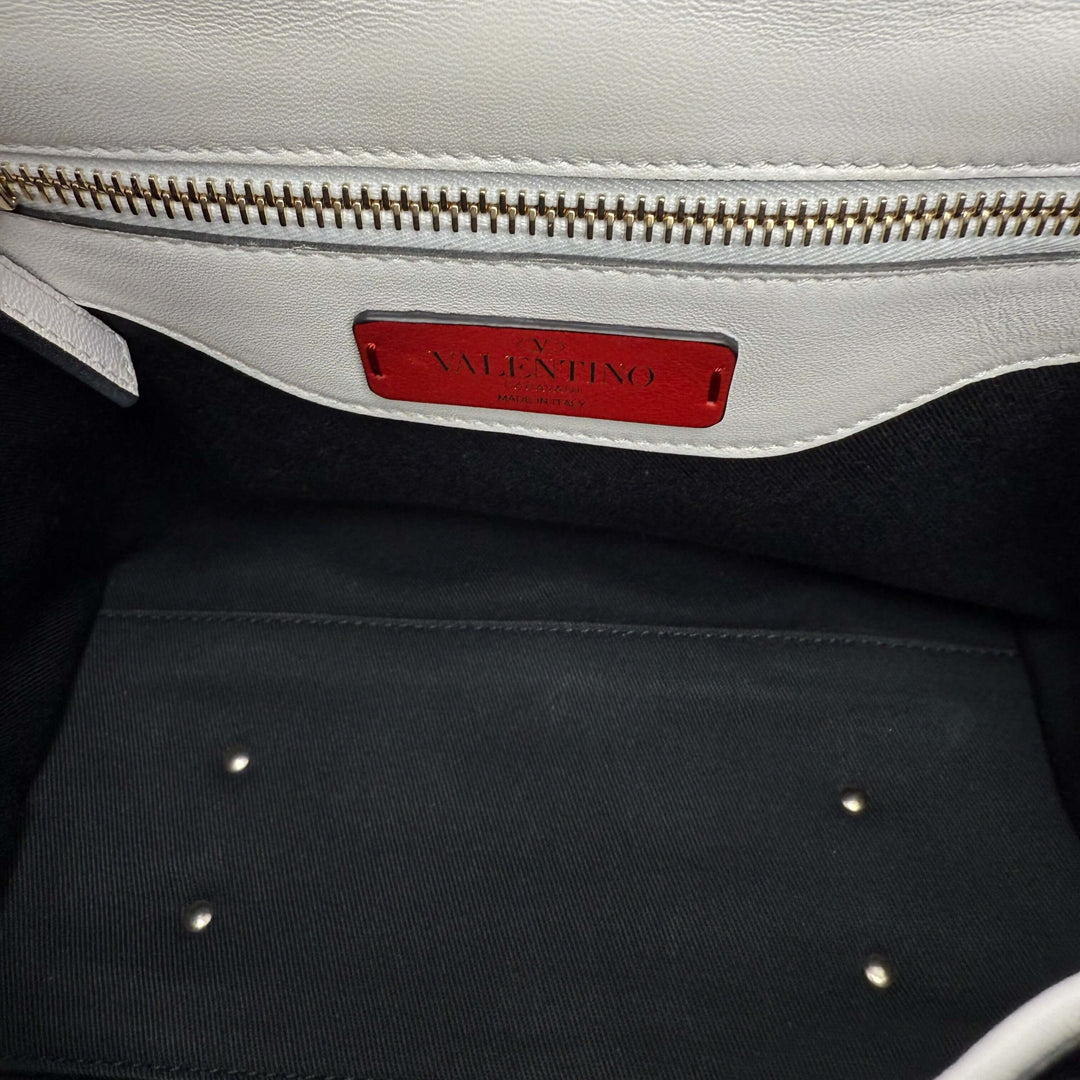 Interior view of Valentino Garavani Nappa Medium Candystud Top Handle Bag, showcasing the red logo tag and elegant lining.